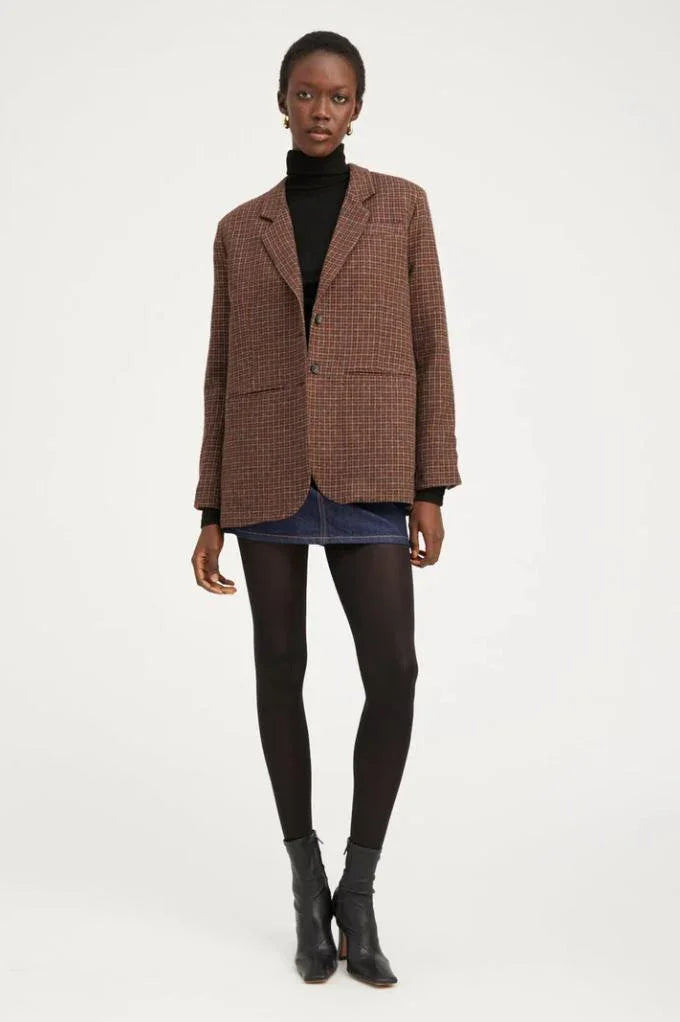 Woman wearing oversized brown plaid blazer, black turtleneck, mini skirt, black tights and ankle boots